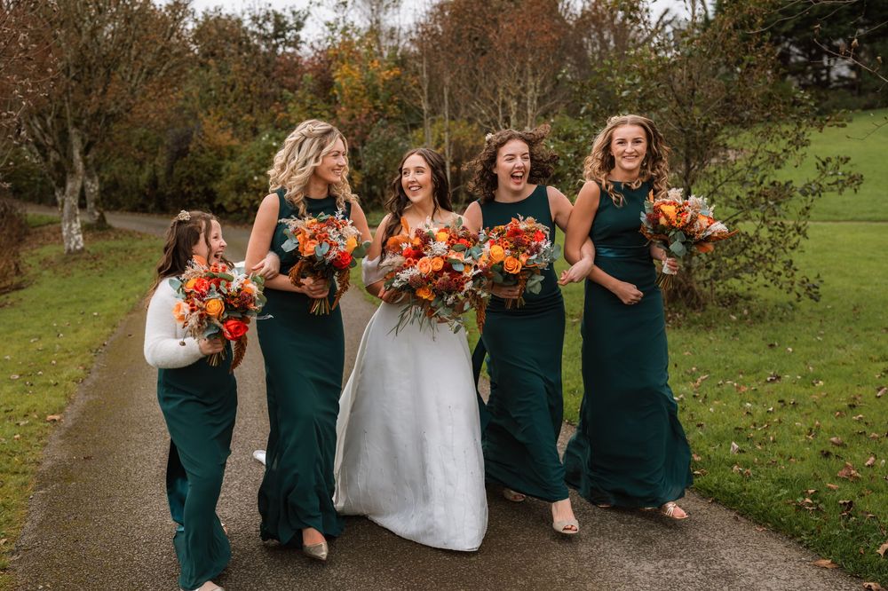Wedding party in emerald green dresses and white gown pose together in autumn outdoor setting.