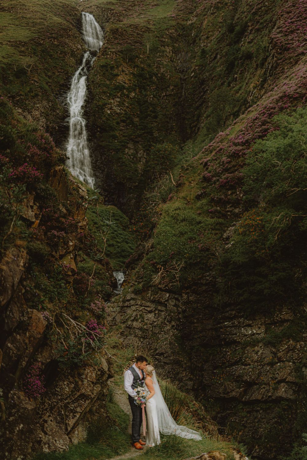 Scenic waterfall cascades down rocky cliff face surrounded by lush green forest.