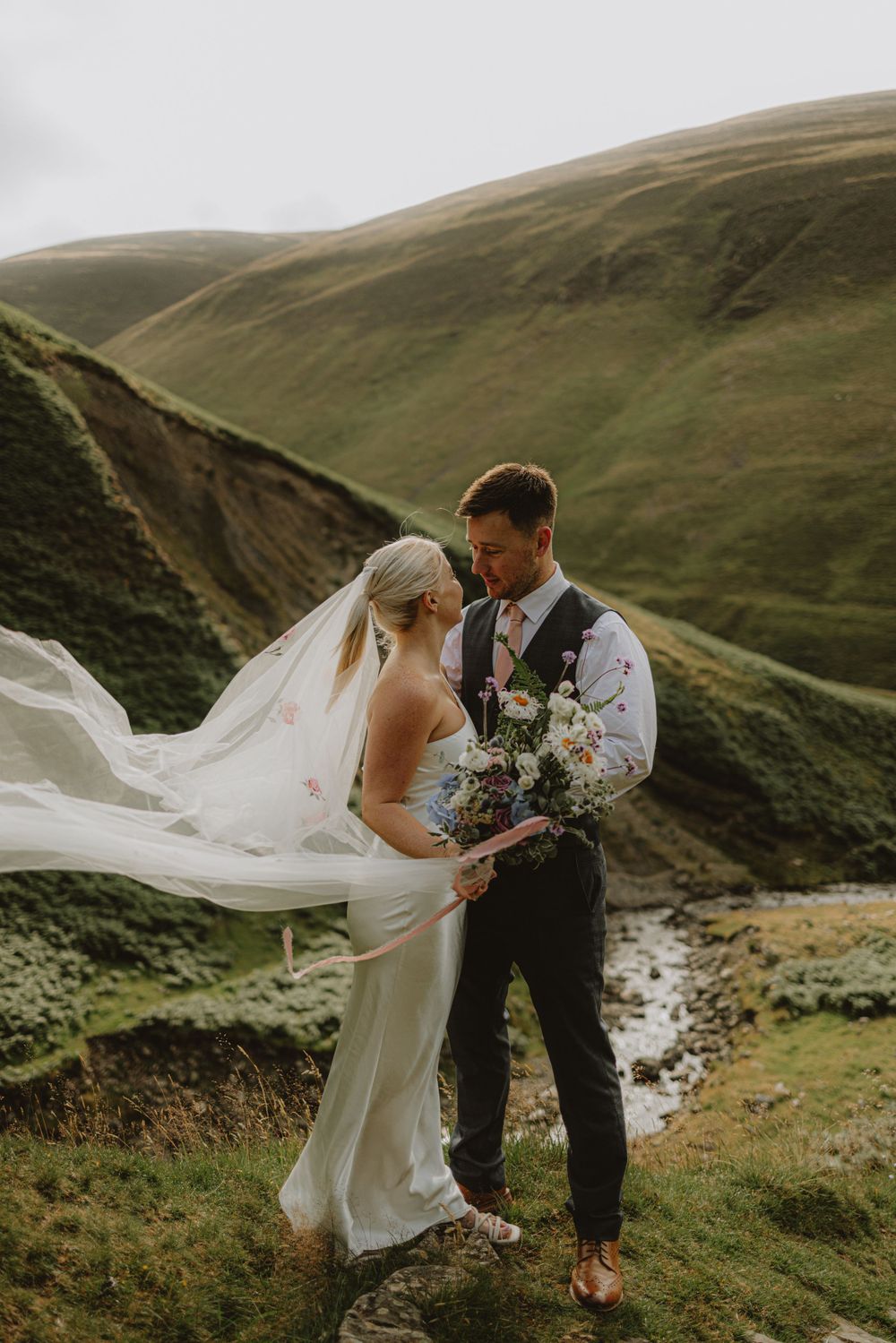 A romantic wedding photoshoot in the rolling green hills with a flowing veil catching the wind.