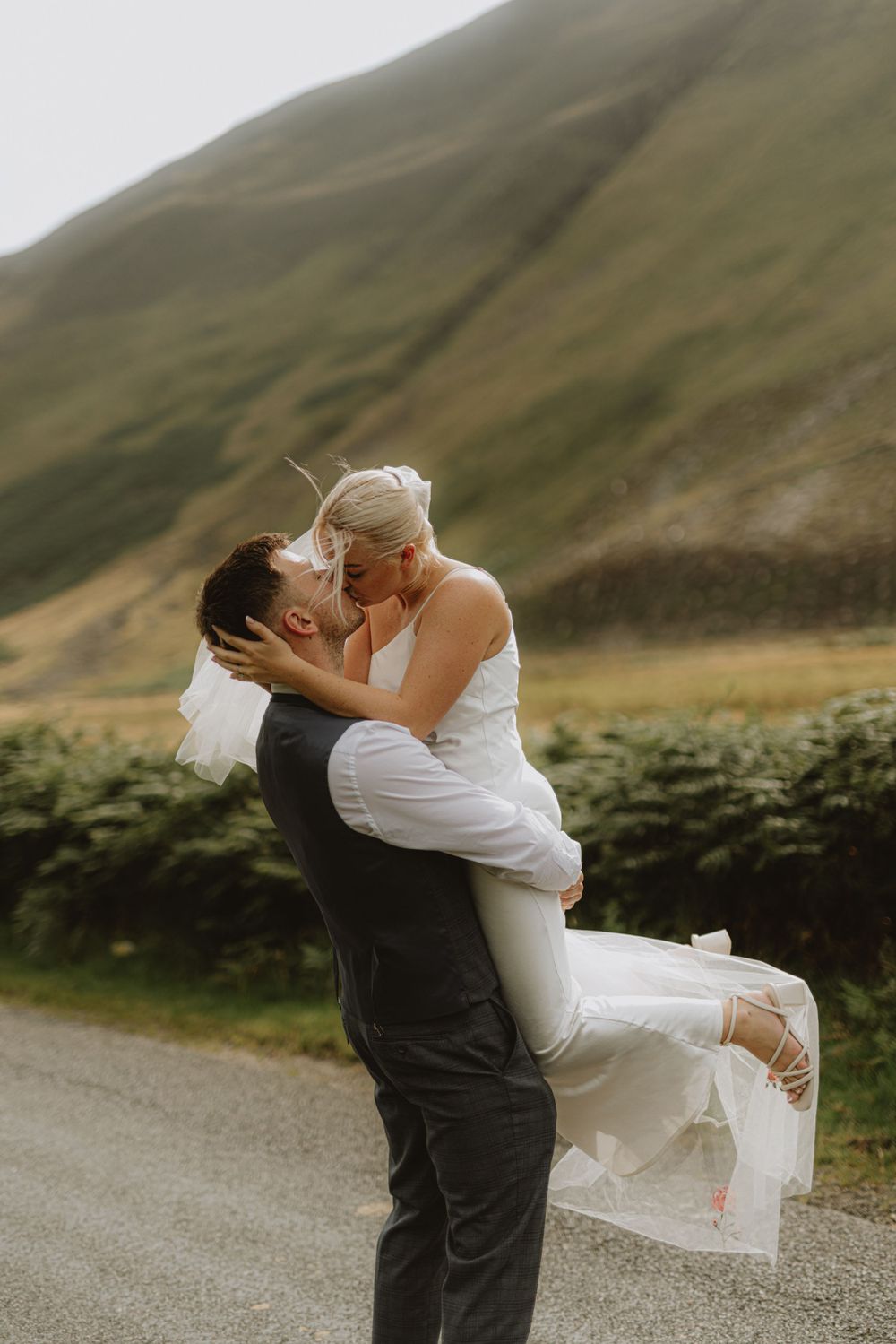 Joyful wedding couple embraces in a dramatic lift against mountain scenery.