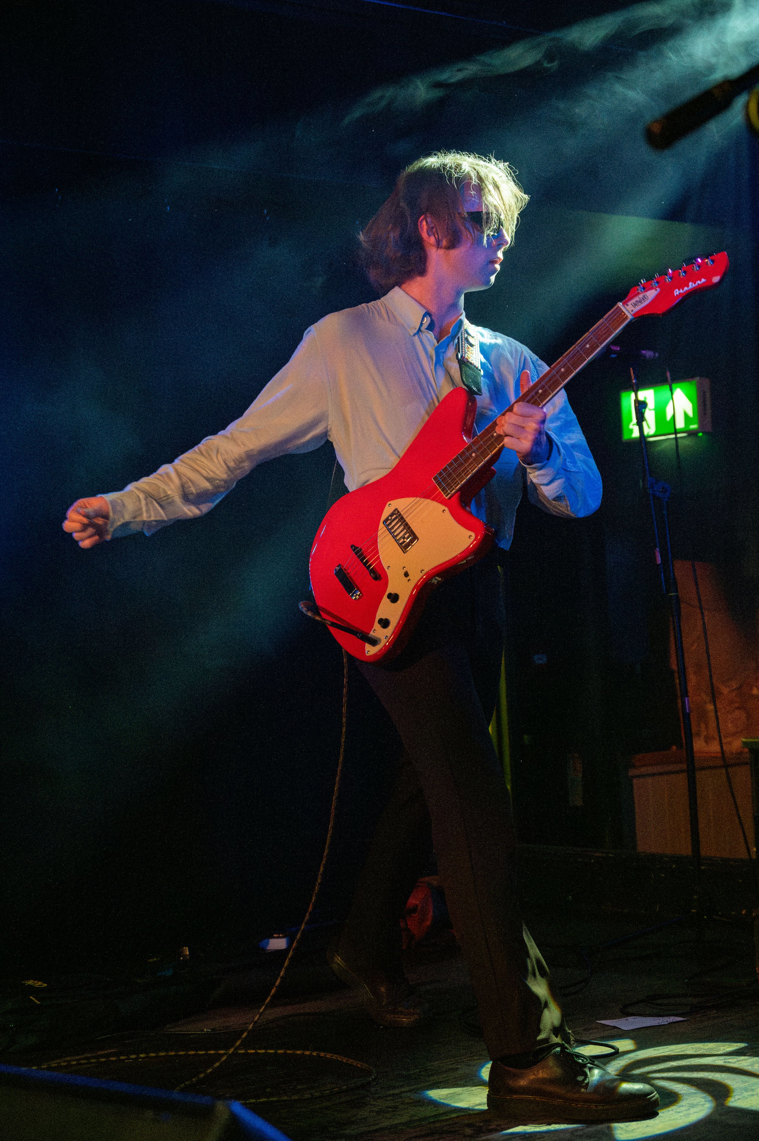 Musician playing a bright red electric guitar on stage with dramatic backlighting and smoke effects.