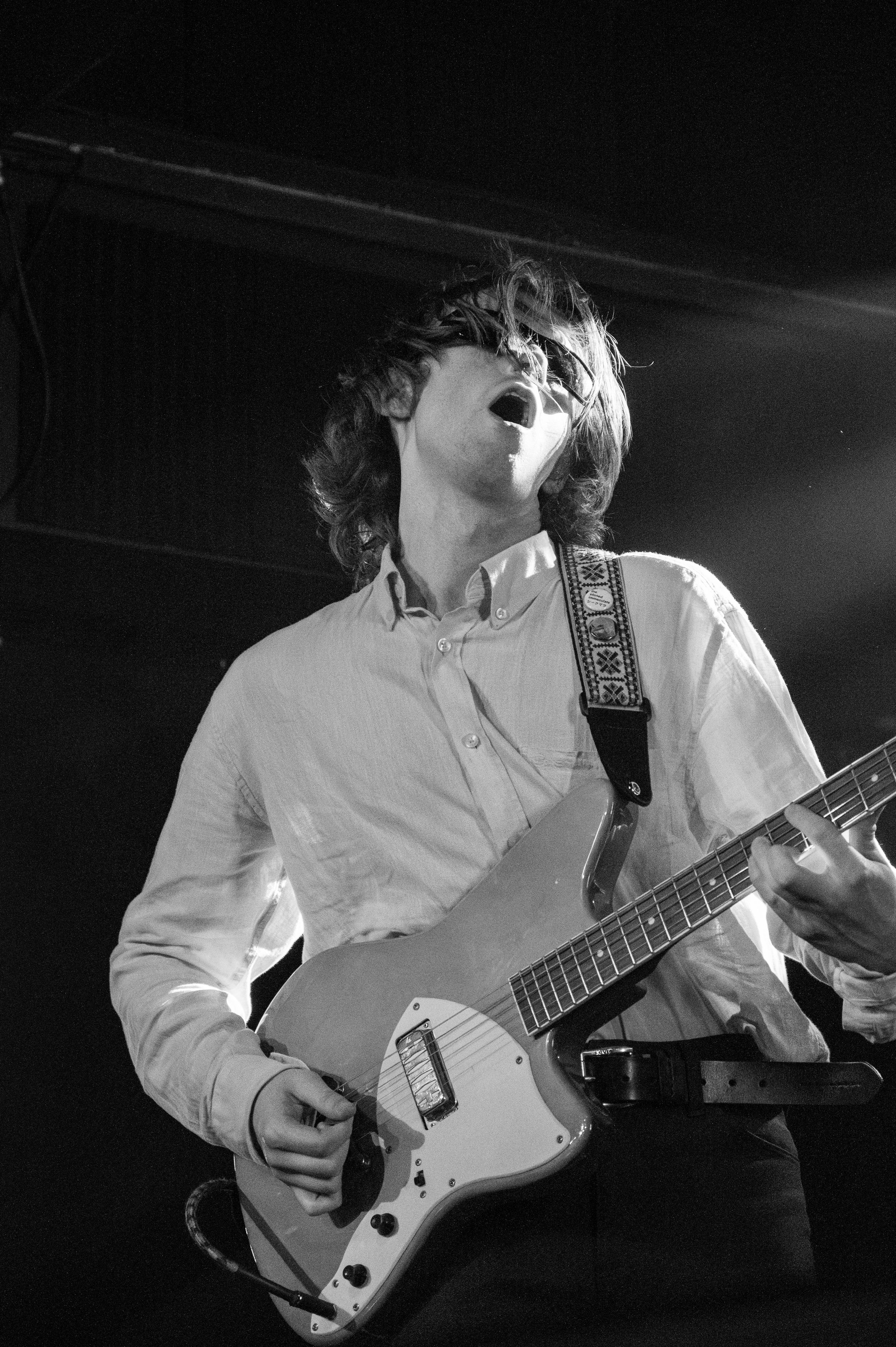 Black and white image of guitarist playing white electric guitar during live performance.