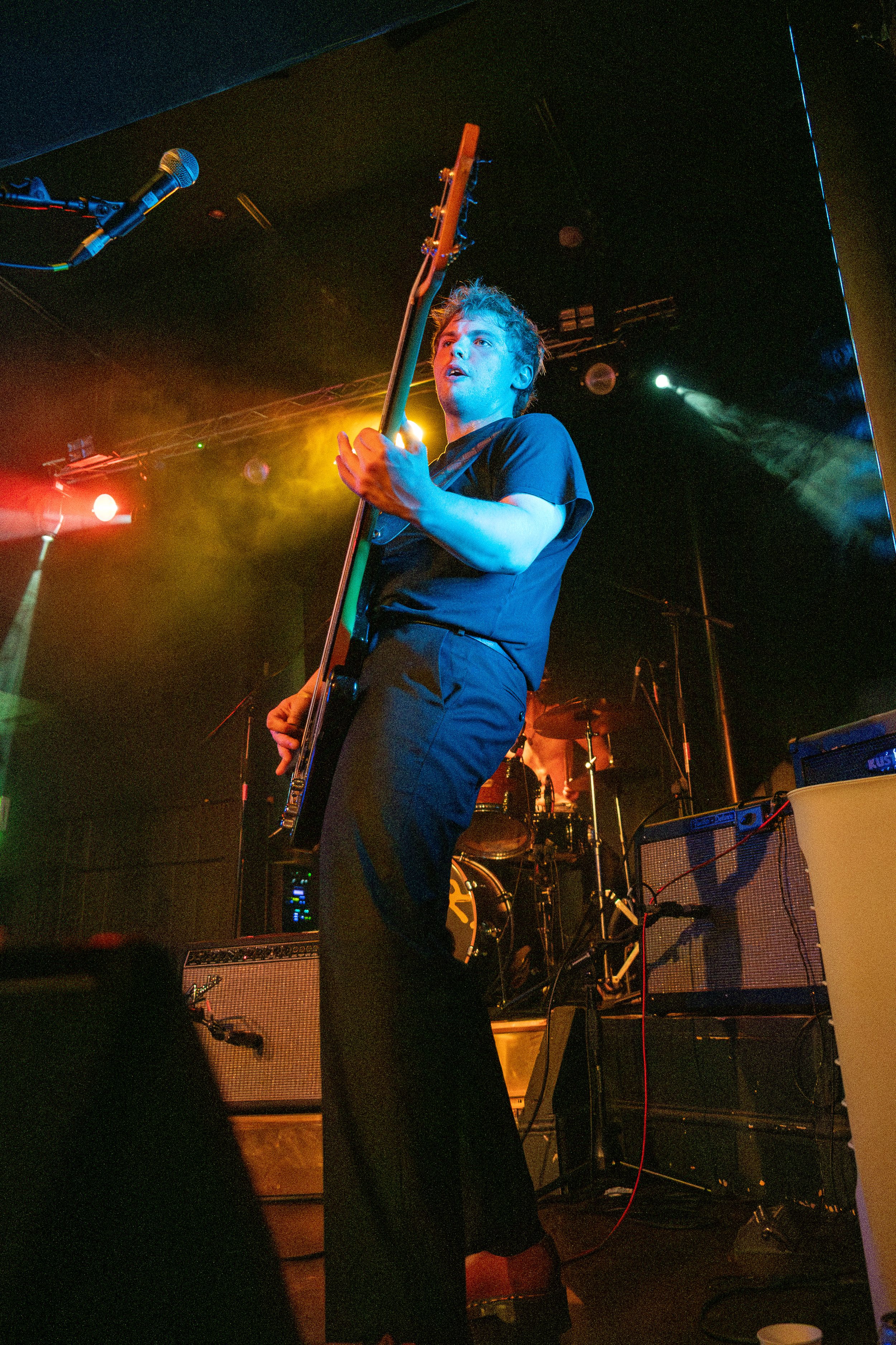 Bass player performs on stage bathed in dramatic blue and red lighting during an energetic concert performance.