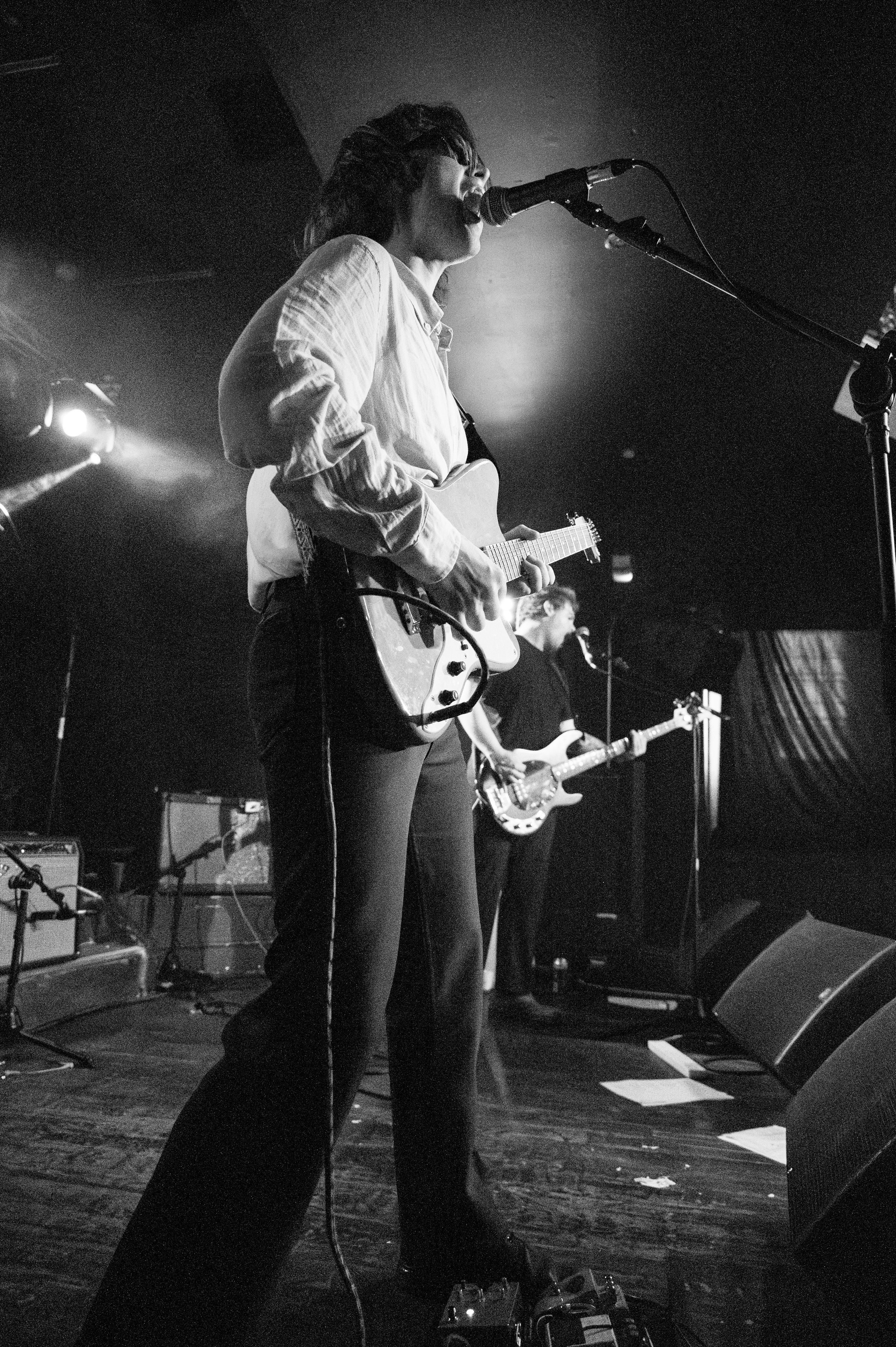 Black and white photo of musician performing with guitar on stage under dramatic lighting.
