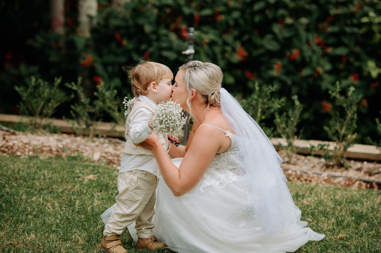 An intimate wedding moment captured in a garden with someone in a white dress and child in formal attire.