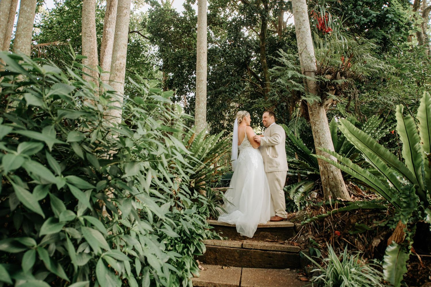 Couple poses on stone steps surrounded by tropical garden foliage.