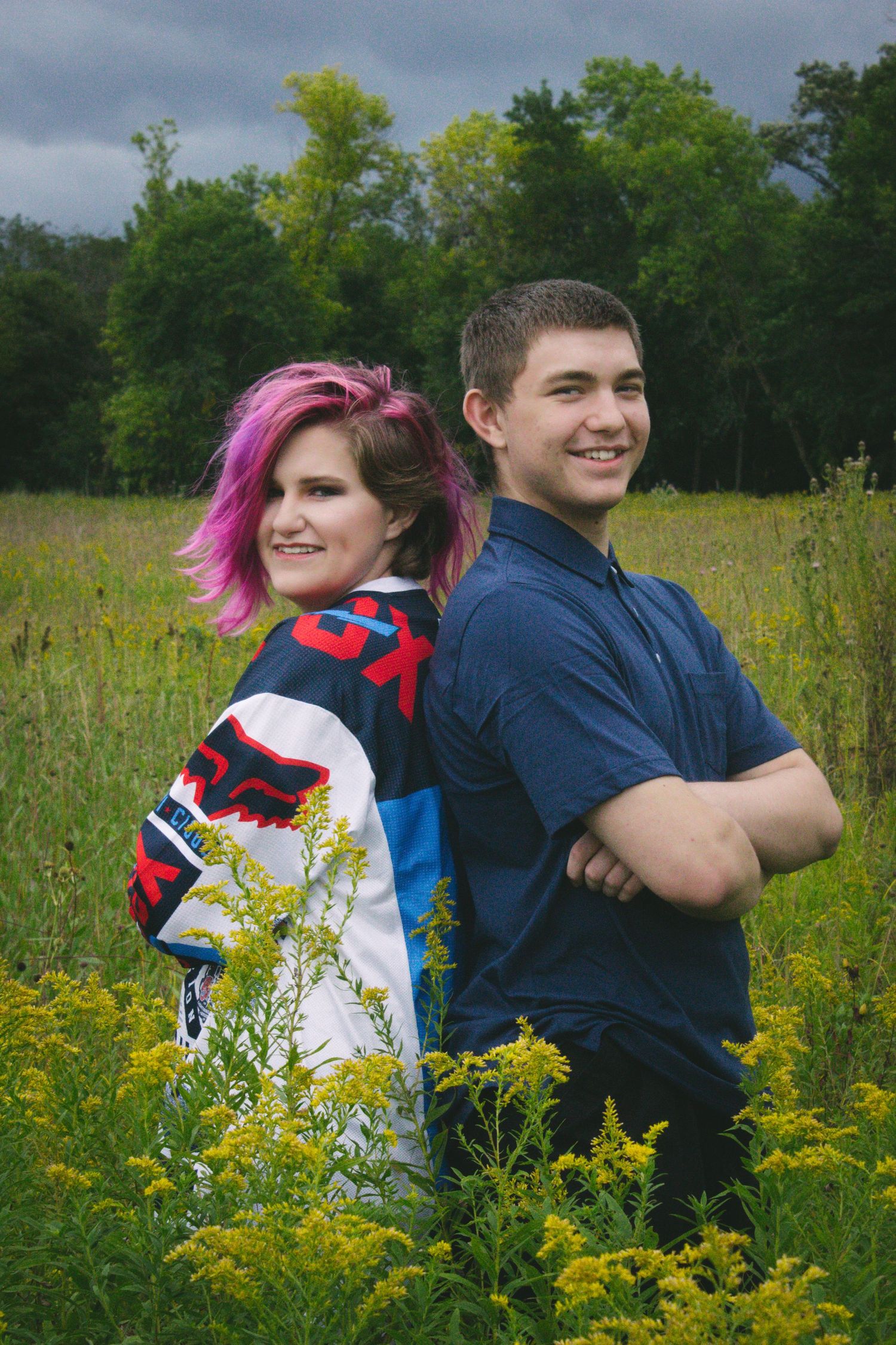 A couple poses back-to-back in a wildflower meadow on an overcast day.