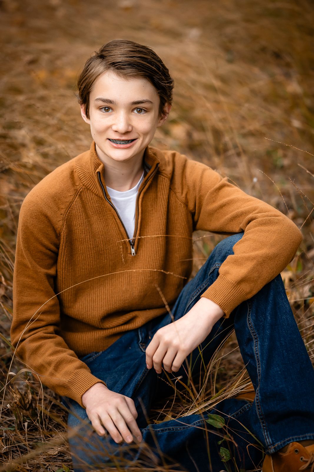 Portrait of young person in brown sweater sitting outdoors in autumn setting.