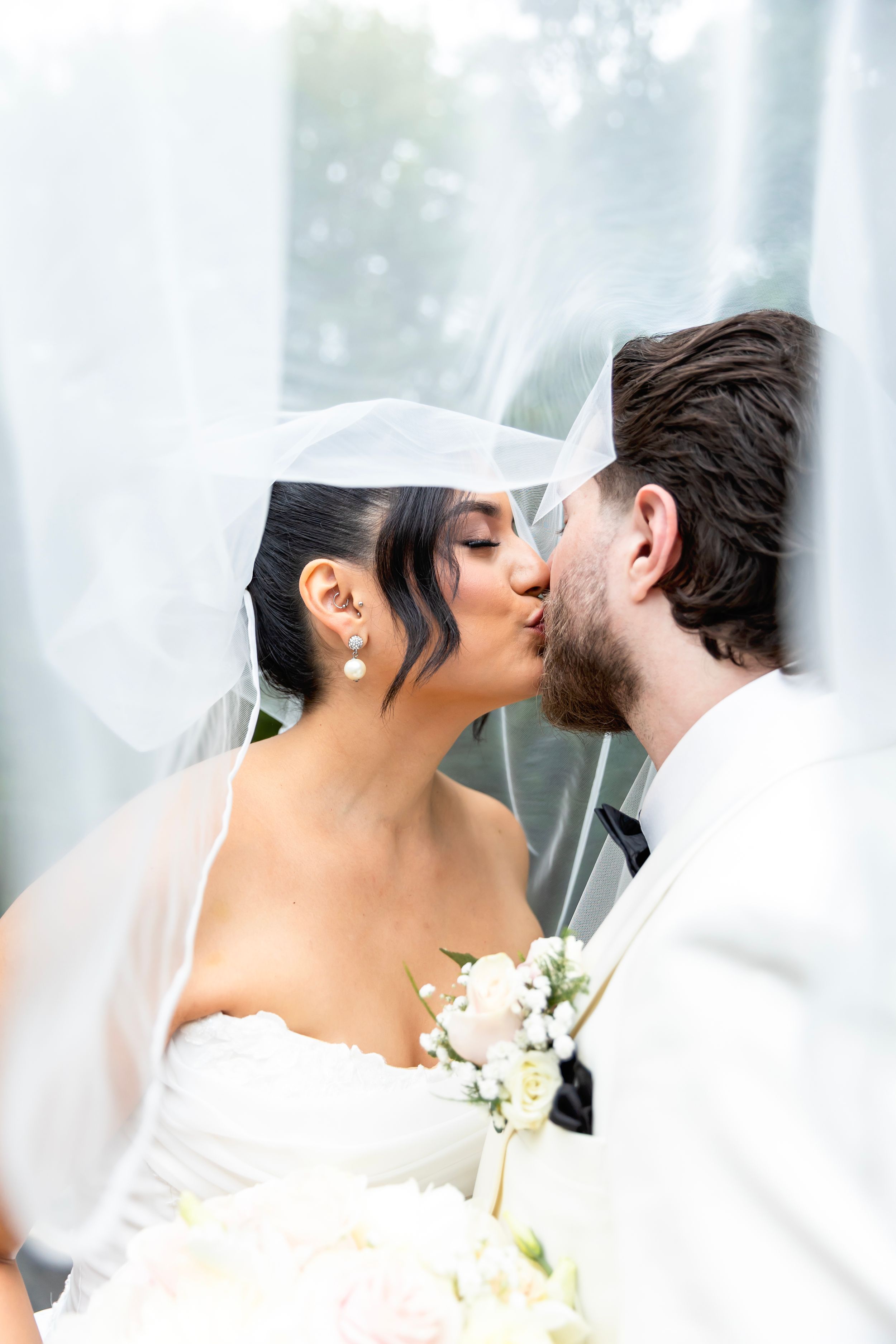 Romantic newlyweds share a tender kiss under a flowing white veil during their wedding ceremony. NJ wedding photographer