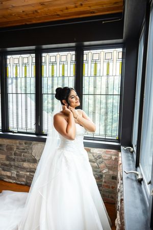 Two people in white wedding dresses stand together in front of large windows with decorative panes.