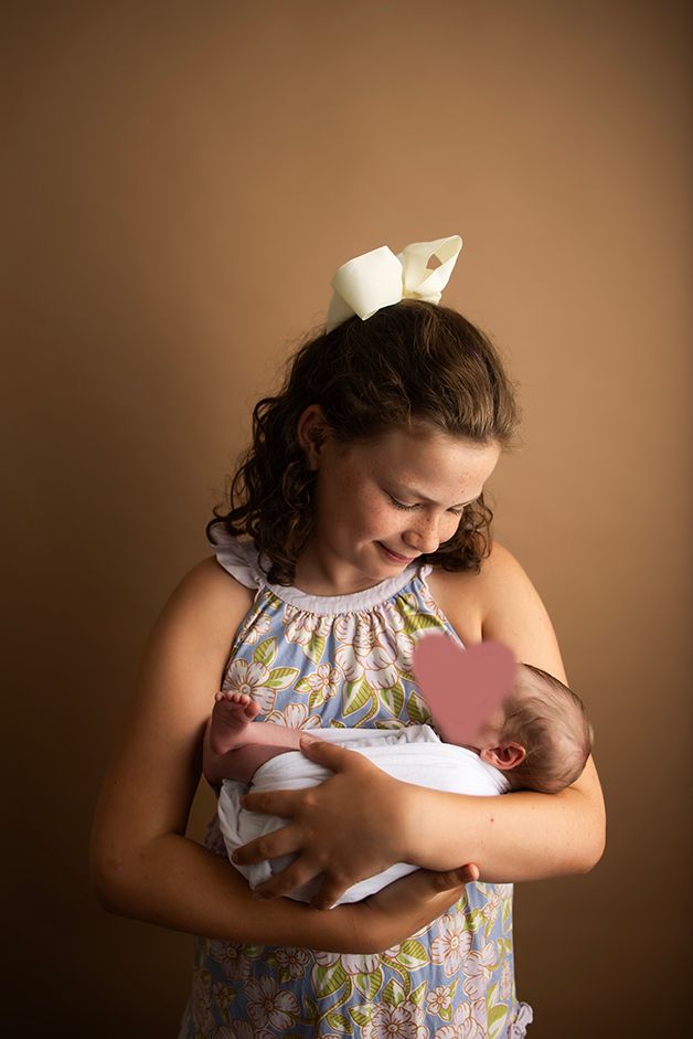Image of a young girl holding her new foster sibling.  She is looking down at them adoringly.