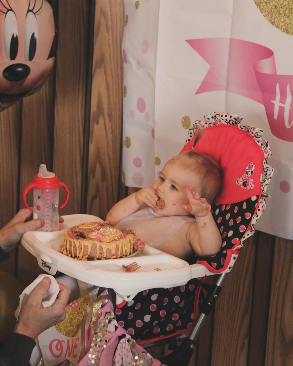 Baby in highchair reaching for birthday cake during first birthday celebration.