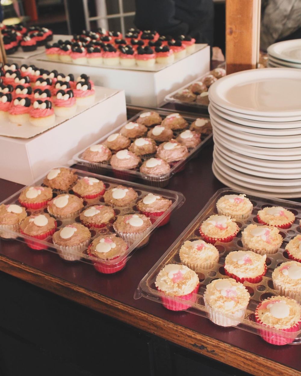 Display of pink frosted cupcakes and desserts arranged on wooden table for party.