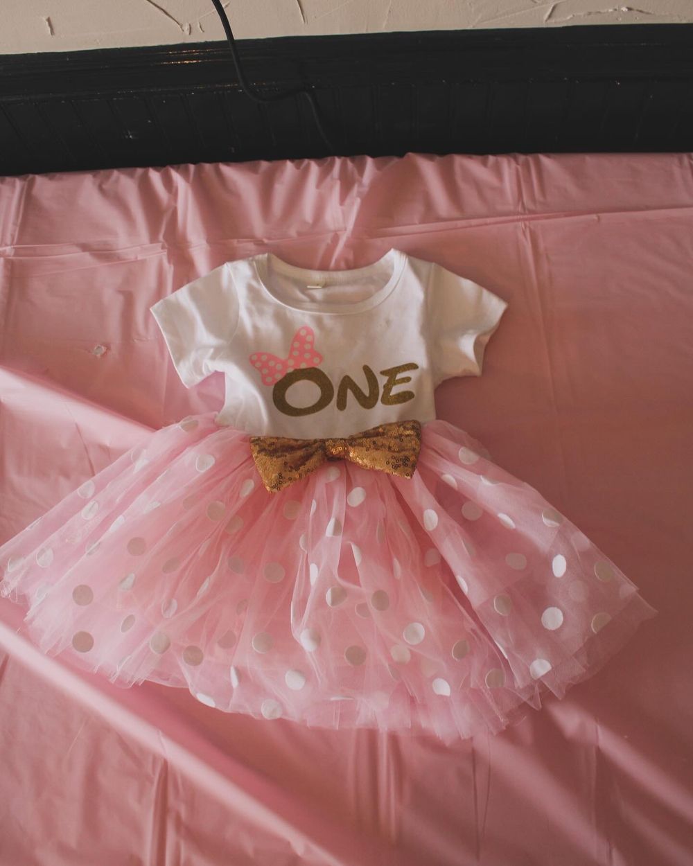 Pink tulle dress with gold 'ONE' text laid flat for first birthday photo.