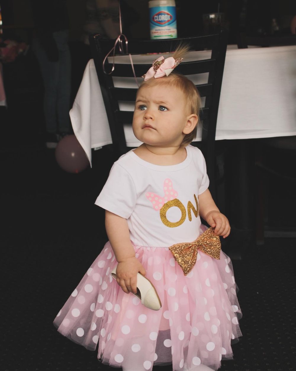 Baby in pink tulle polka dot dress and gold accents at a birthday celebration.