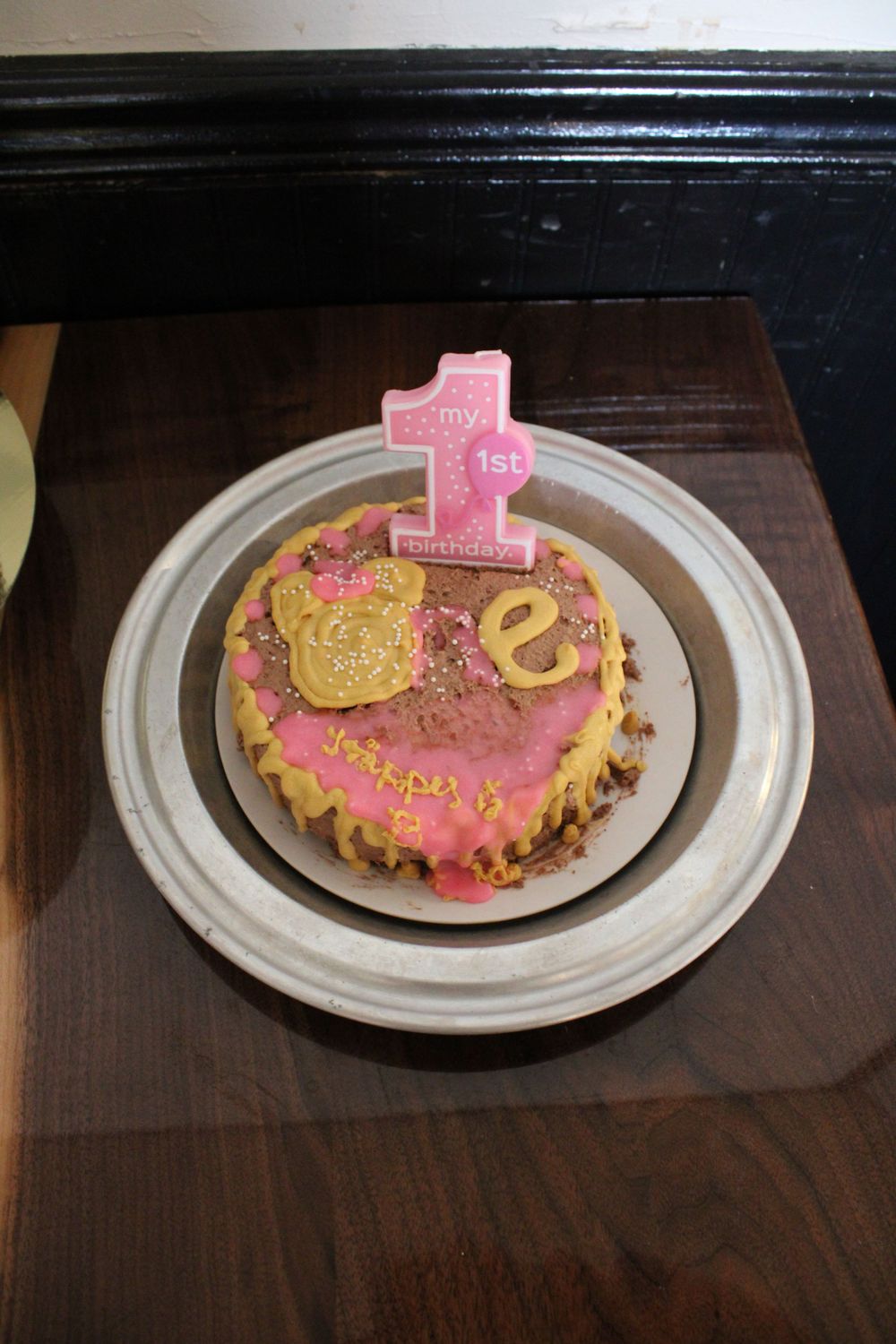 Pink and gold first birthday smash cake with number one topper on a white plate.