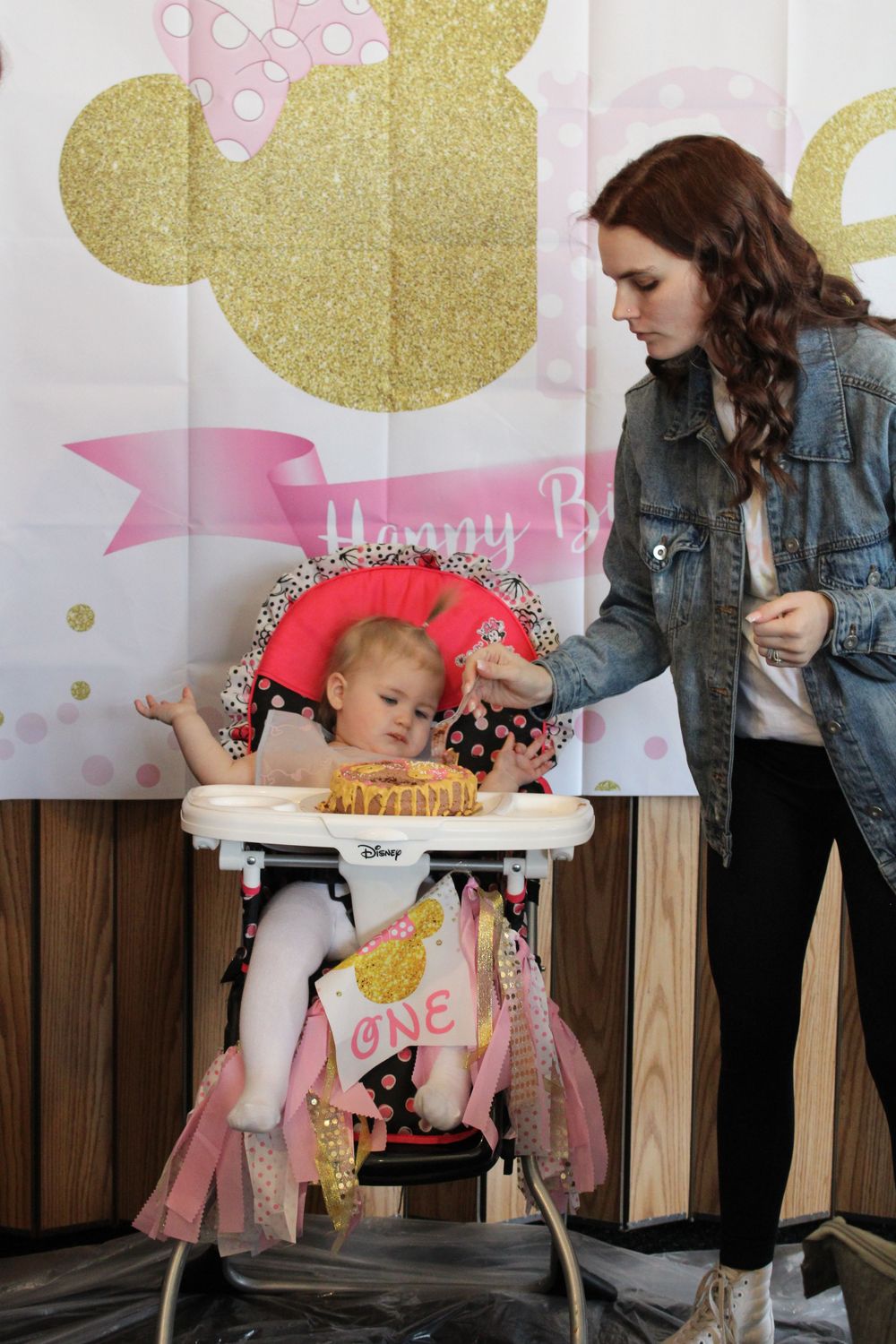 First birthday celebration setup with high chair and pink and gold decorations.