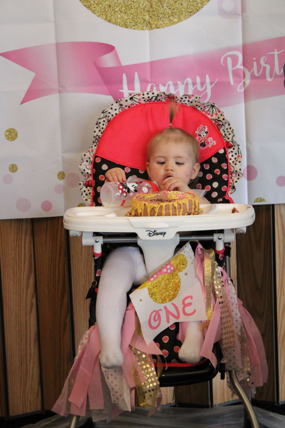 High chair decorated with pink and gold banners and birthday decorations.
