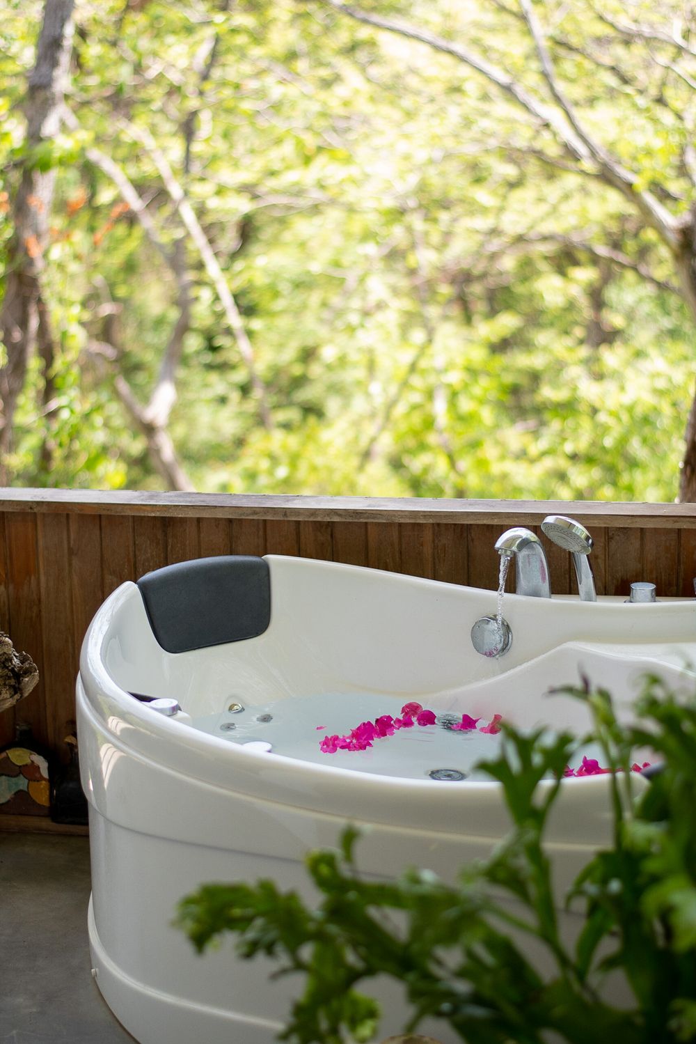 A luxurious white jacuzzi tub decorated with pink flowers on a deck surrounded by greenery.