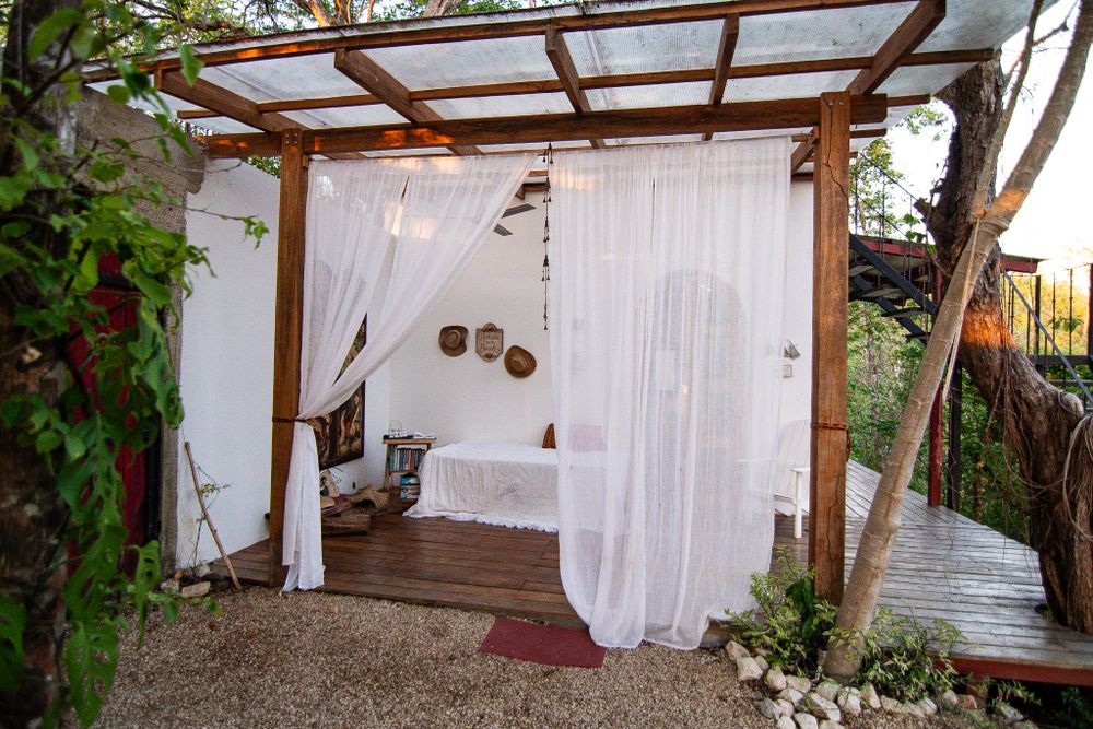 Cozy outdoor sleeping space with white curtains and wooden pergola roof.
