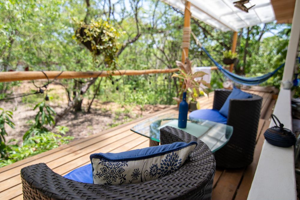 A cozy outdoor seating area with wicker furniture and blue cushions on a wooden deck overlooking nature.
