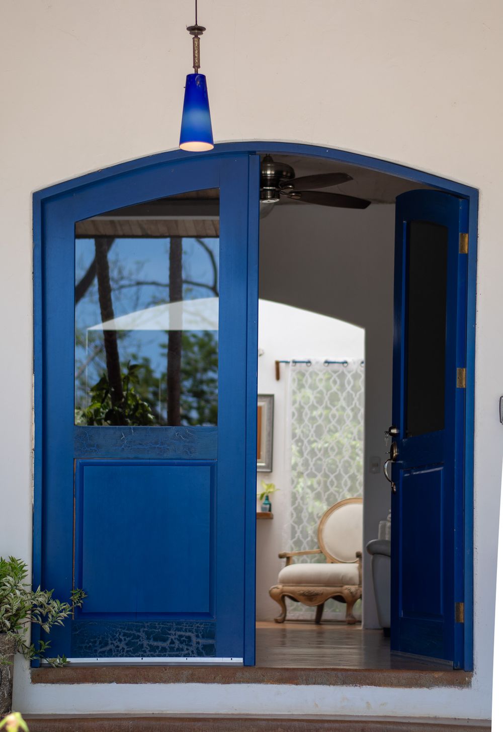 A striking blue arched doorway with glass panels and pendant light leading into an interior space.