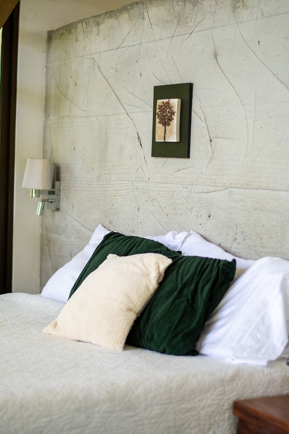 A minimalist bedroom with white bedding, green pillows, and simple framed artwork on a textured wall.