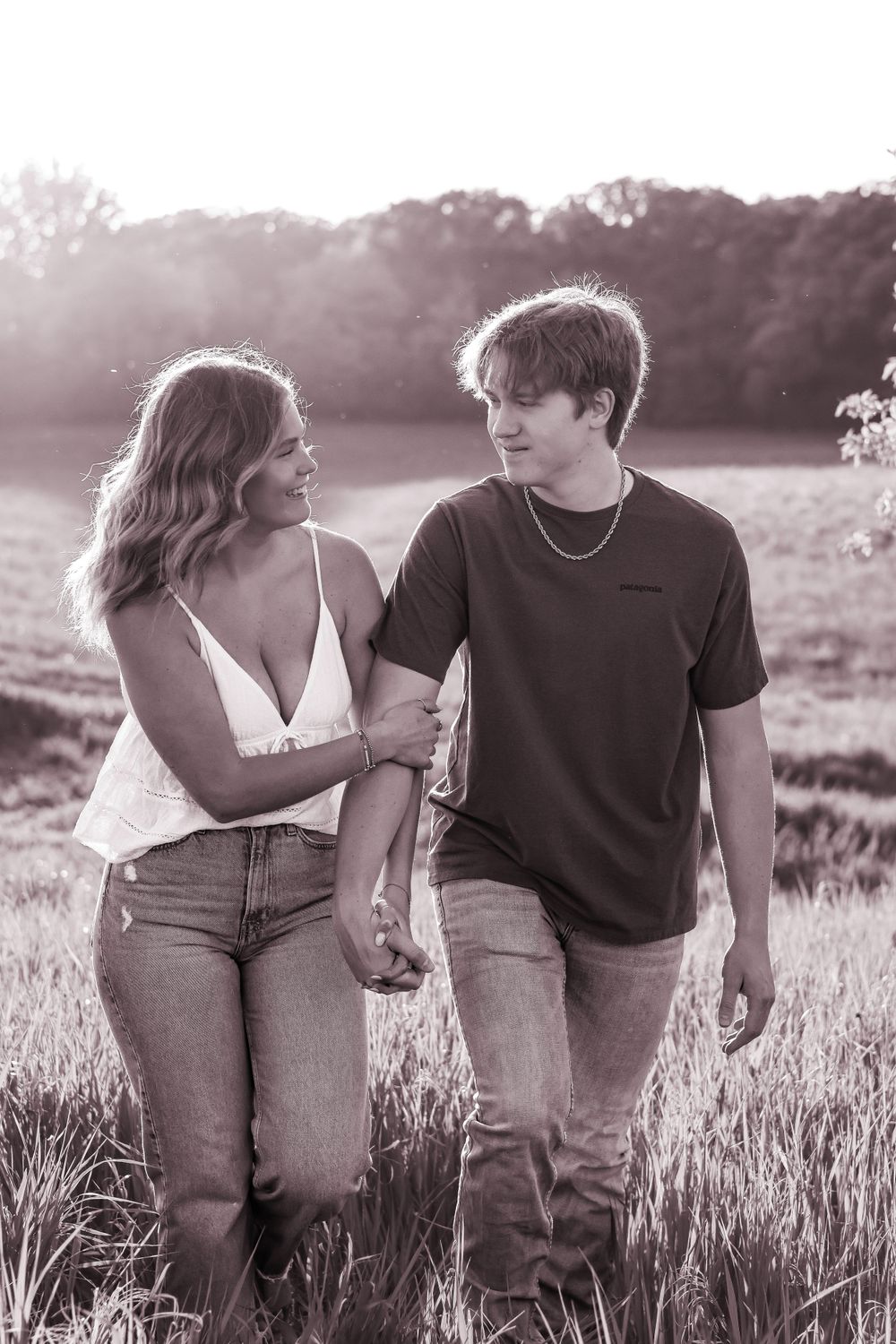 A couple walks hand in hand through a sunlit meadow at golden hour.