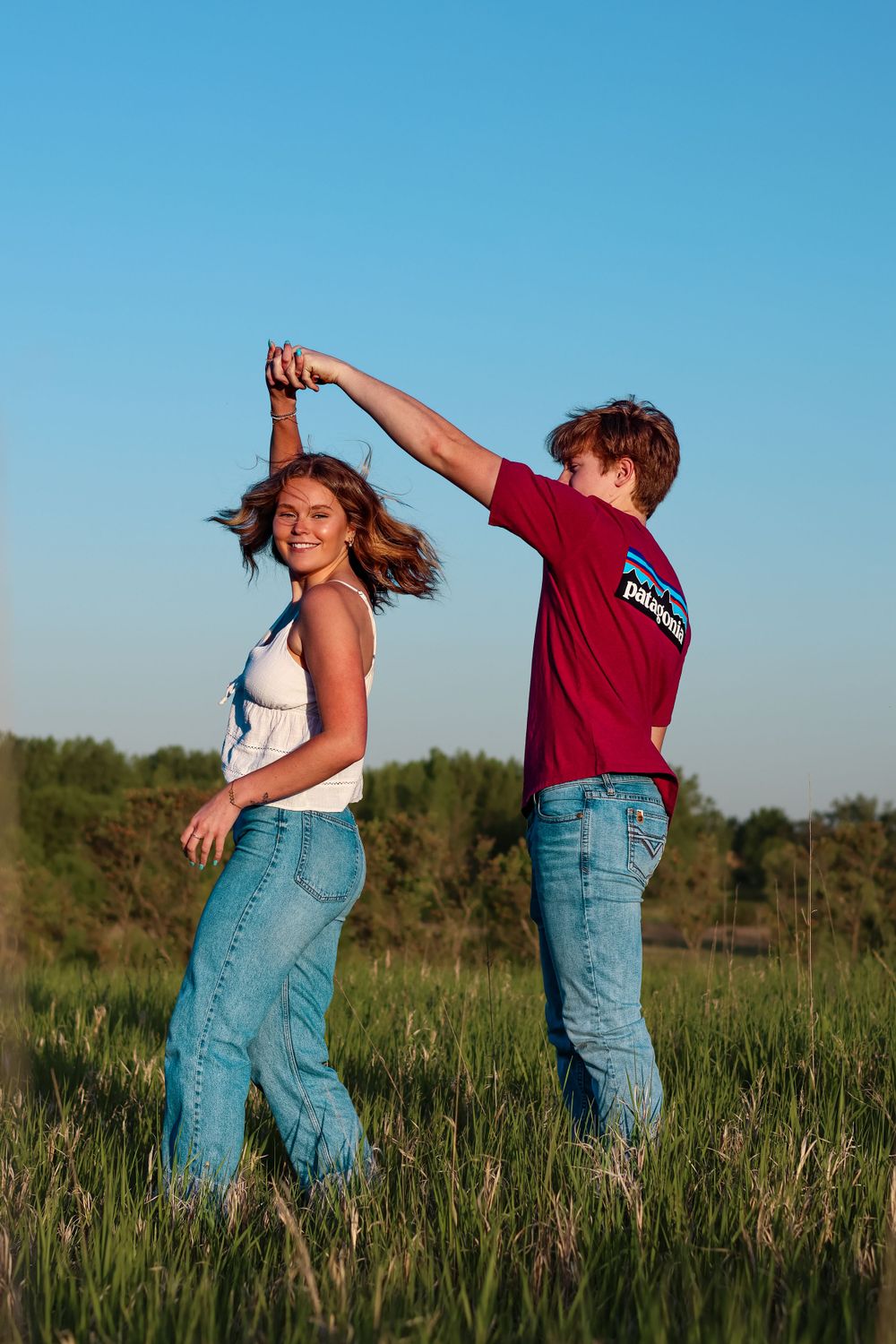 A couple dances playfully in a field during golden hour.
