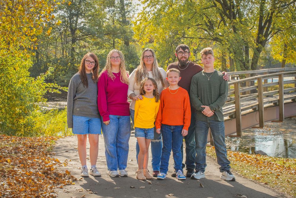A group of people pose together on a wooden walkway surrounded by vibrant fall foliage on an autumn day.