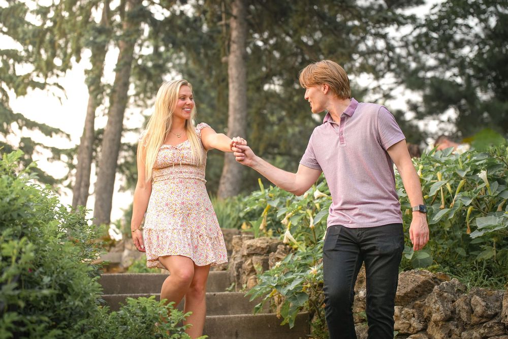 Couple walking together through a lush garden path holding hands during a romantic outdoor engagement photo session.