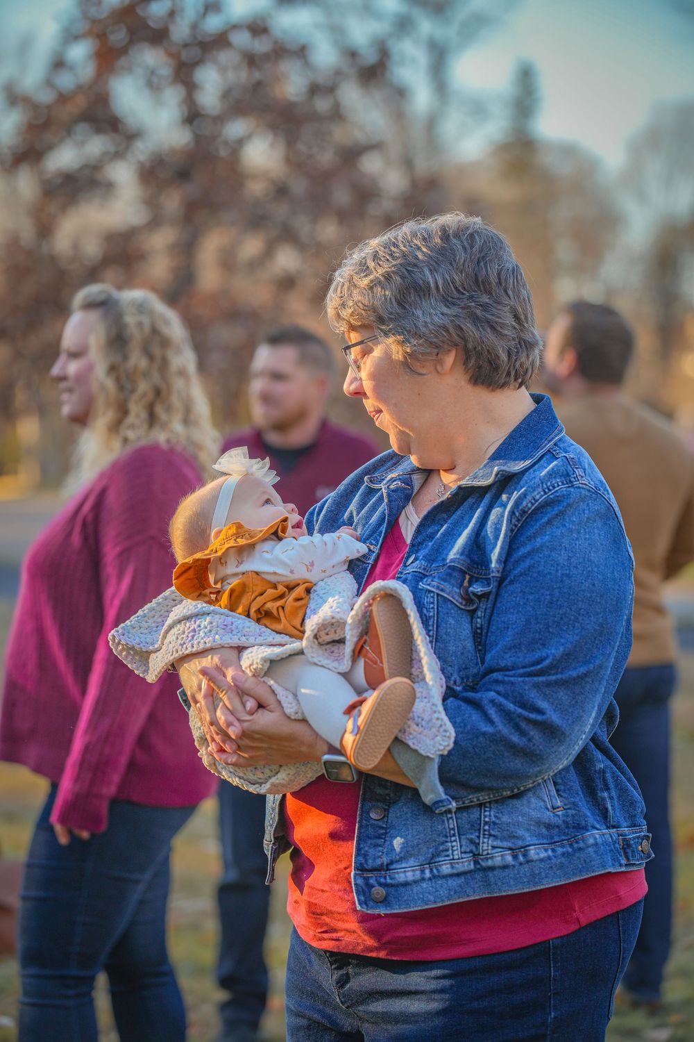 Person in denim jacket and orange shirt holds a wrapped bundle outdoors during golden hour lighting.