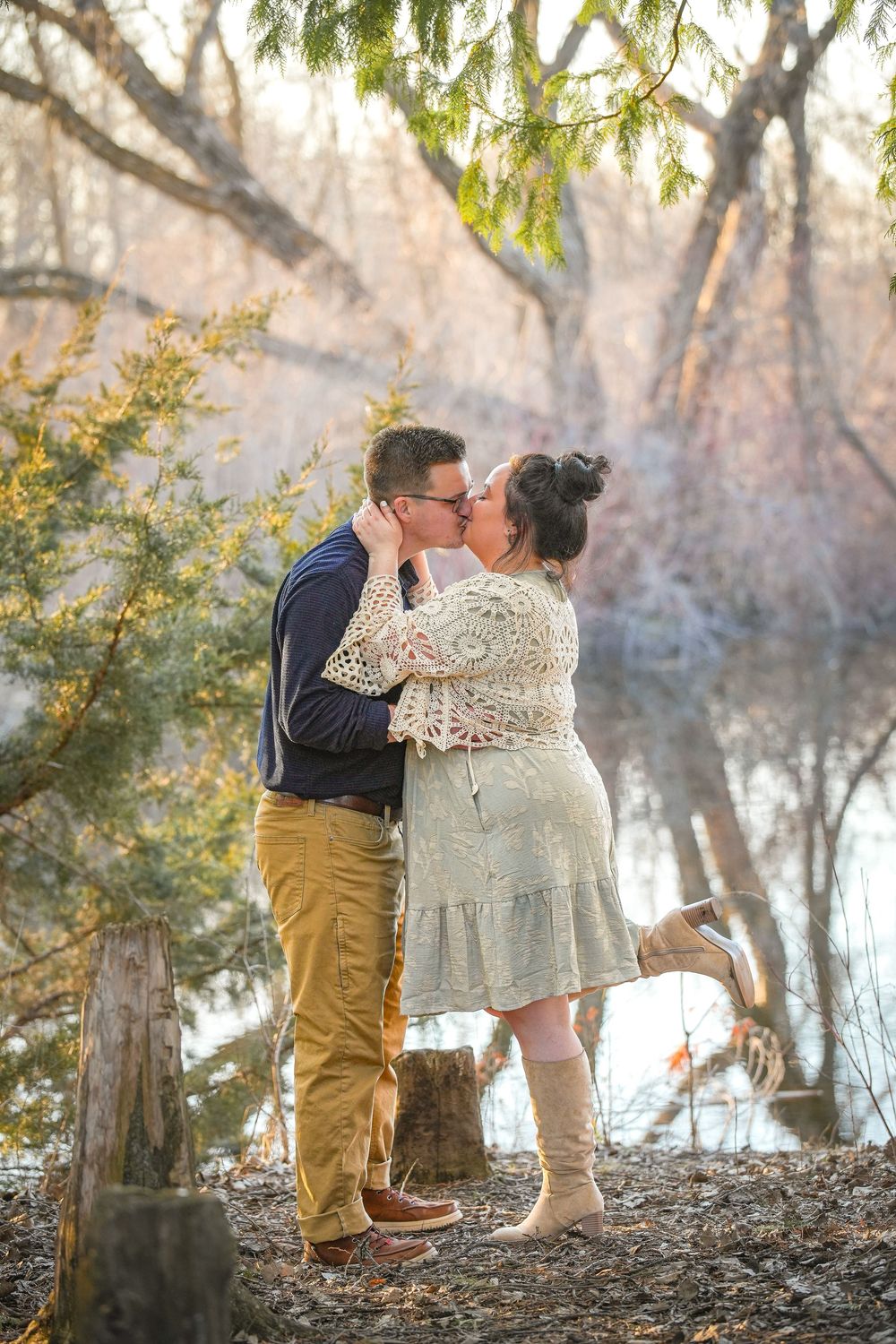 Couple sharing a tender kiss near a serene woodland pond surrounded by autumn trees.