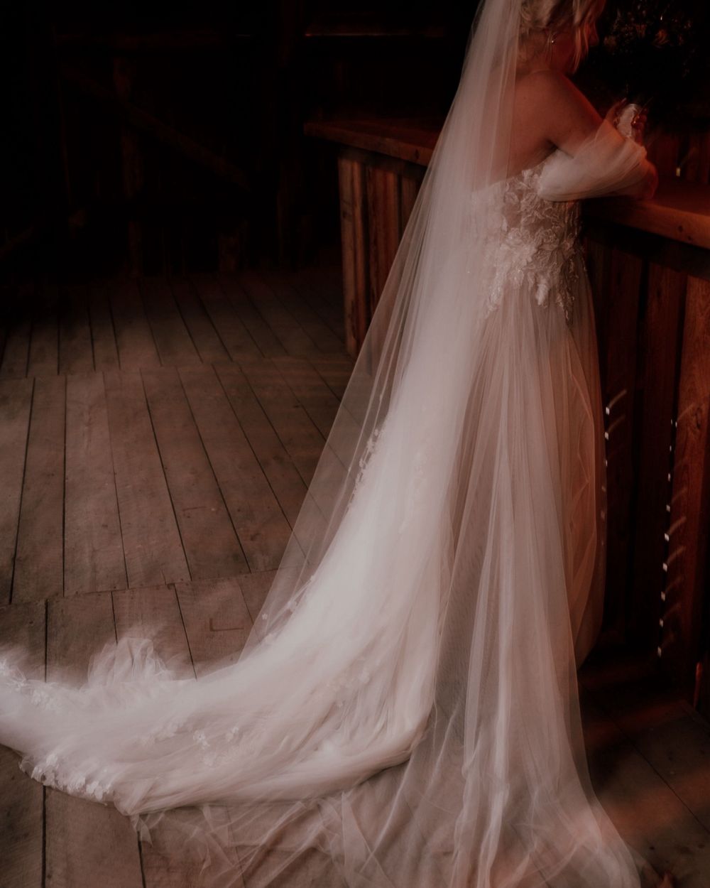 Elegant white wedding dress with long flowing veil and train captures dramatic lighting on rustic wooden floorboards. Une robe de mariée