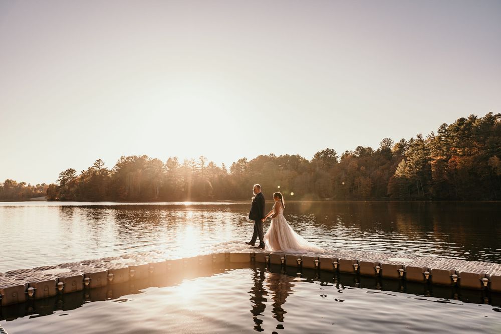 Silhouetted figures stand on a misty dock at sunset as golden light reflects off the calm lake waters.