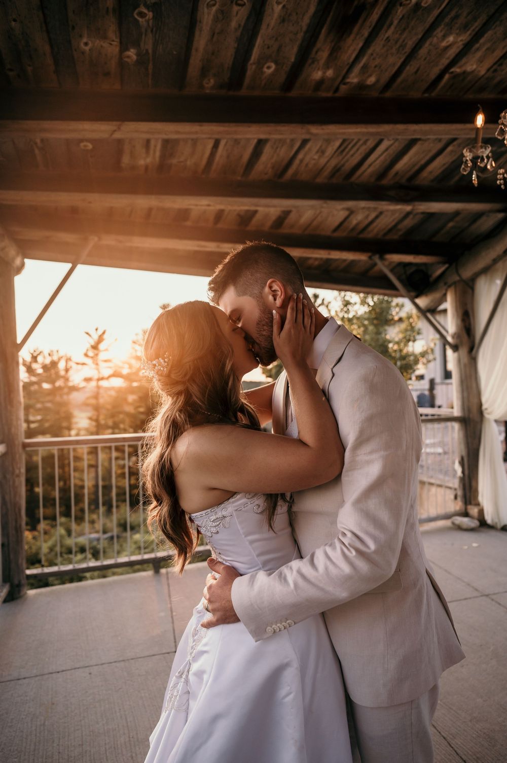 A romantic couple shares an intimate embrace under a rustic wooden overhang at sunset.