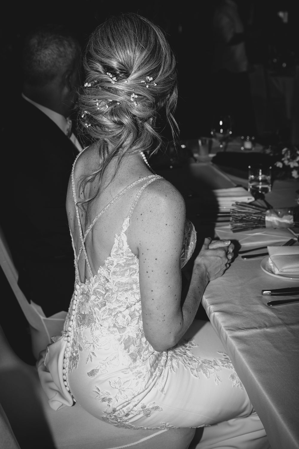 Close-up details of delicate white lace and buttons on the back of a wedding dress at a formal reception.