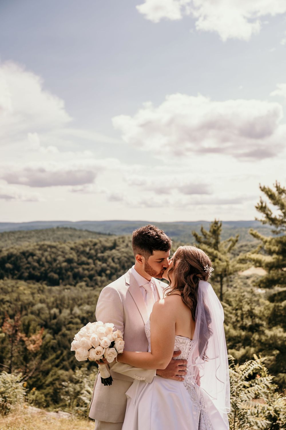 Elegant wedding couple shares an intimate moment on a scenic mountaintop overlooking a lush forest landscape on their special day.