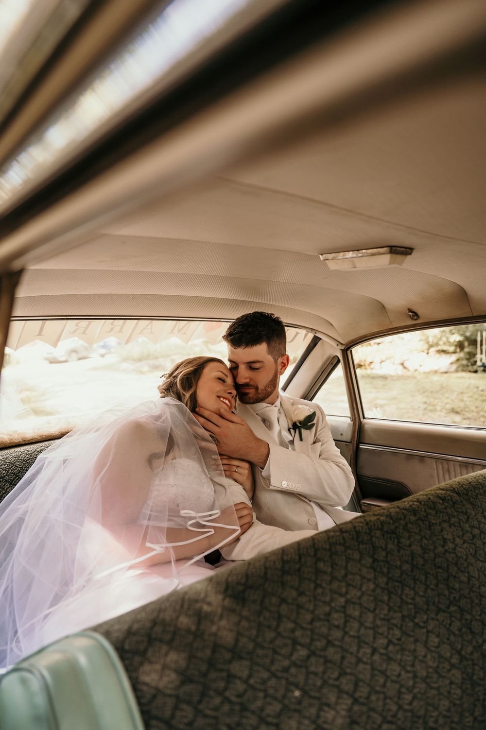 Couple sharing an intimate moment in the backseat of a vintage car with a flowing white veil.
