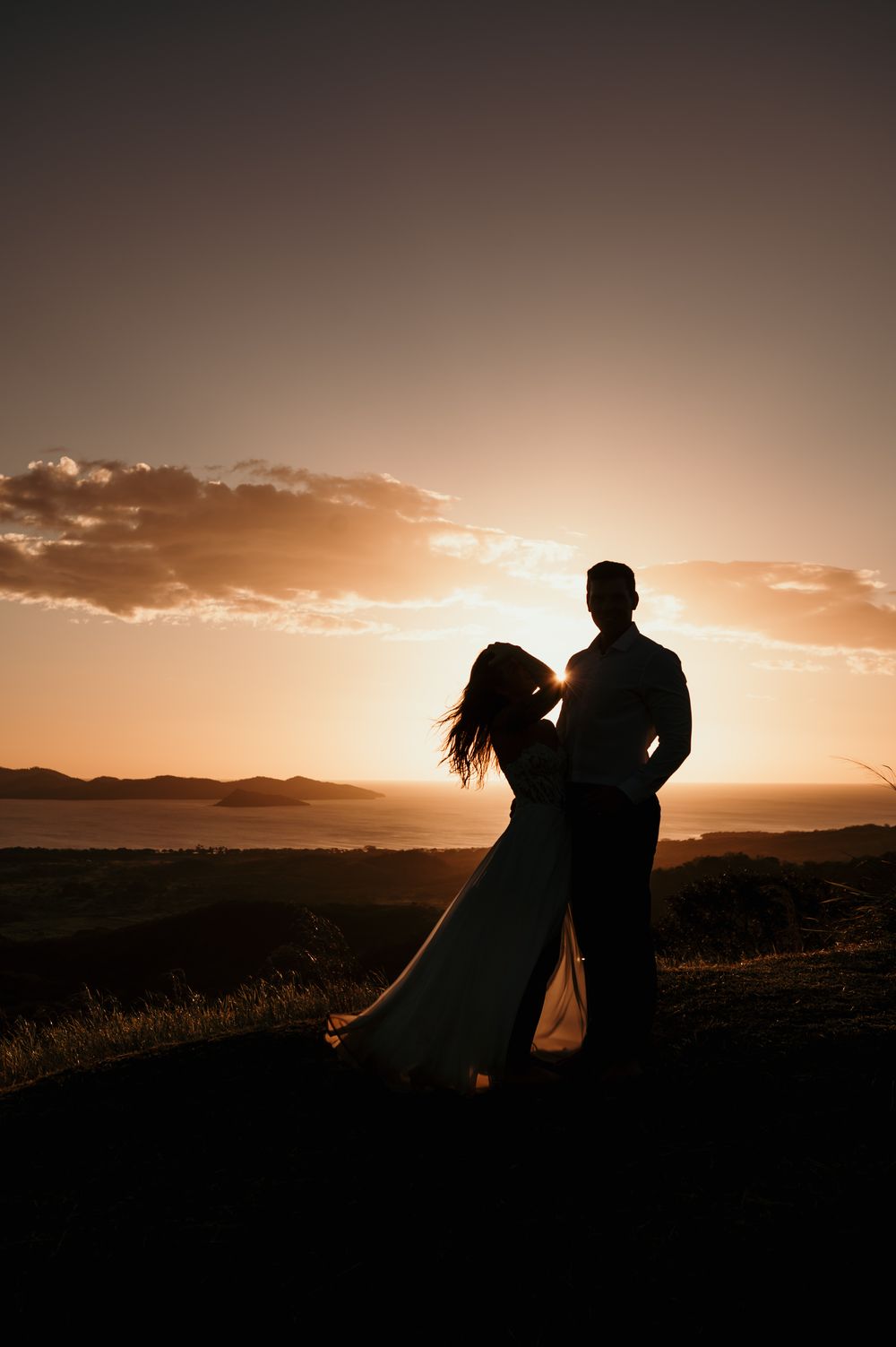 A romantic silhouette of a couple dancing against a golden sunset sky with mountains in the background.