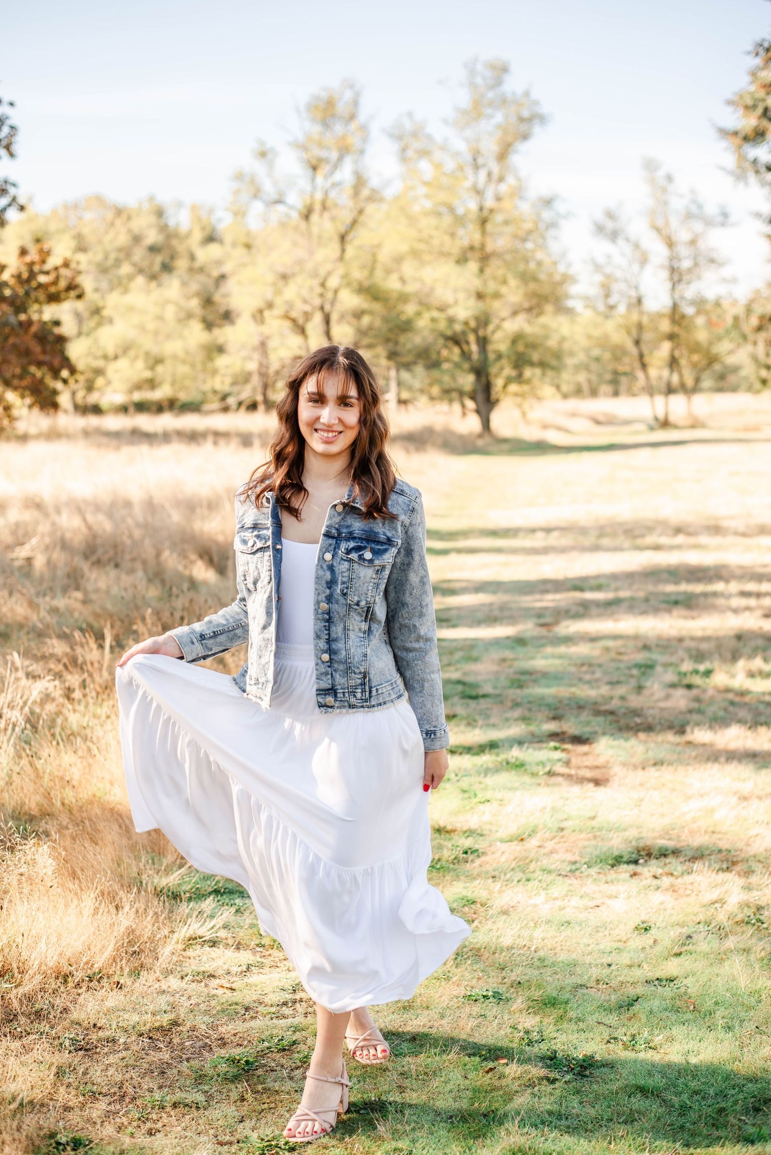 A series of portraits showing someone twirling in a white dress and denim jacket in a sunny outdoor field setting.