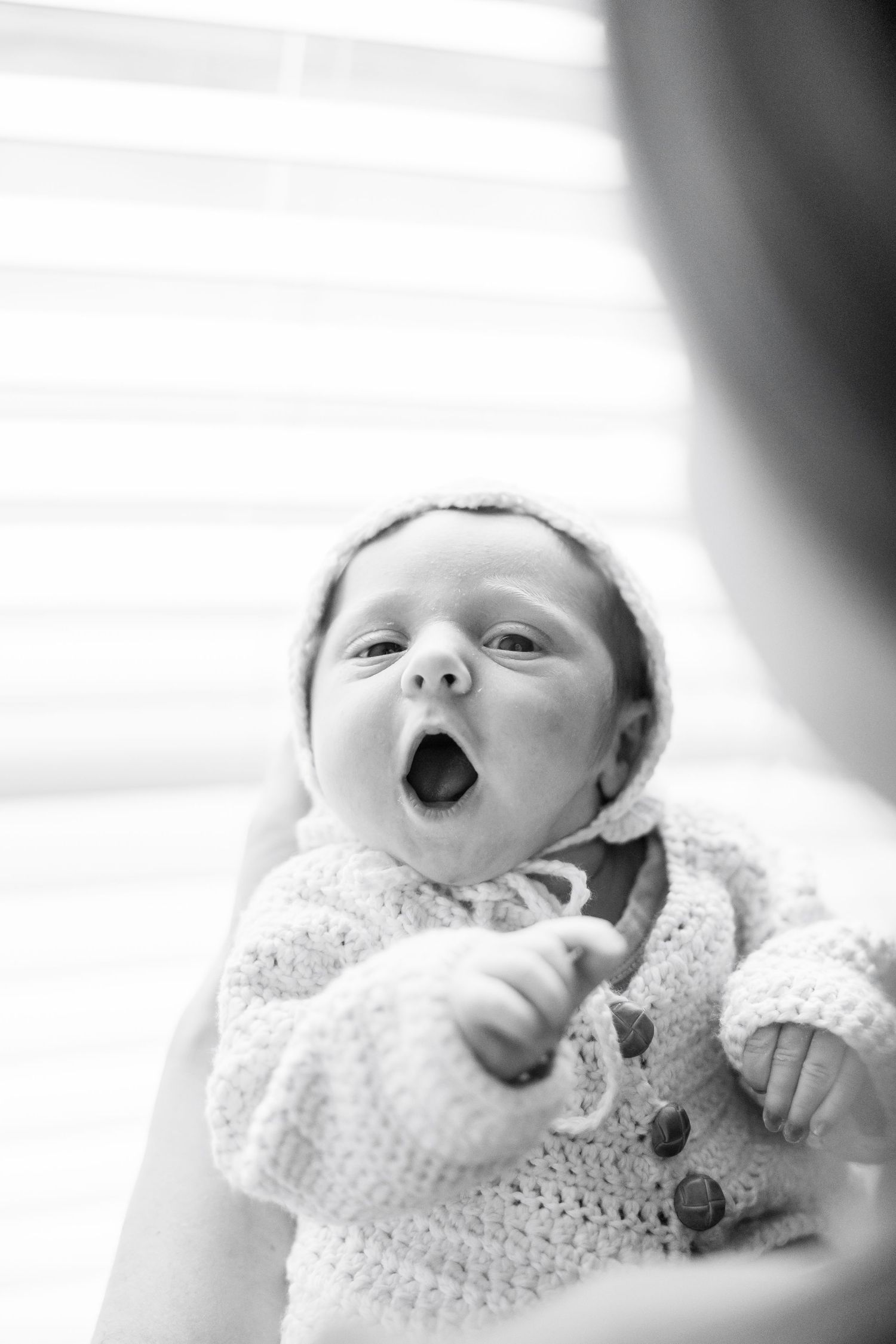 Black and white portrait of a yawning baby wearing a knitted sweater with buttons.