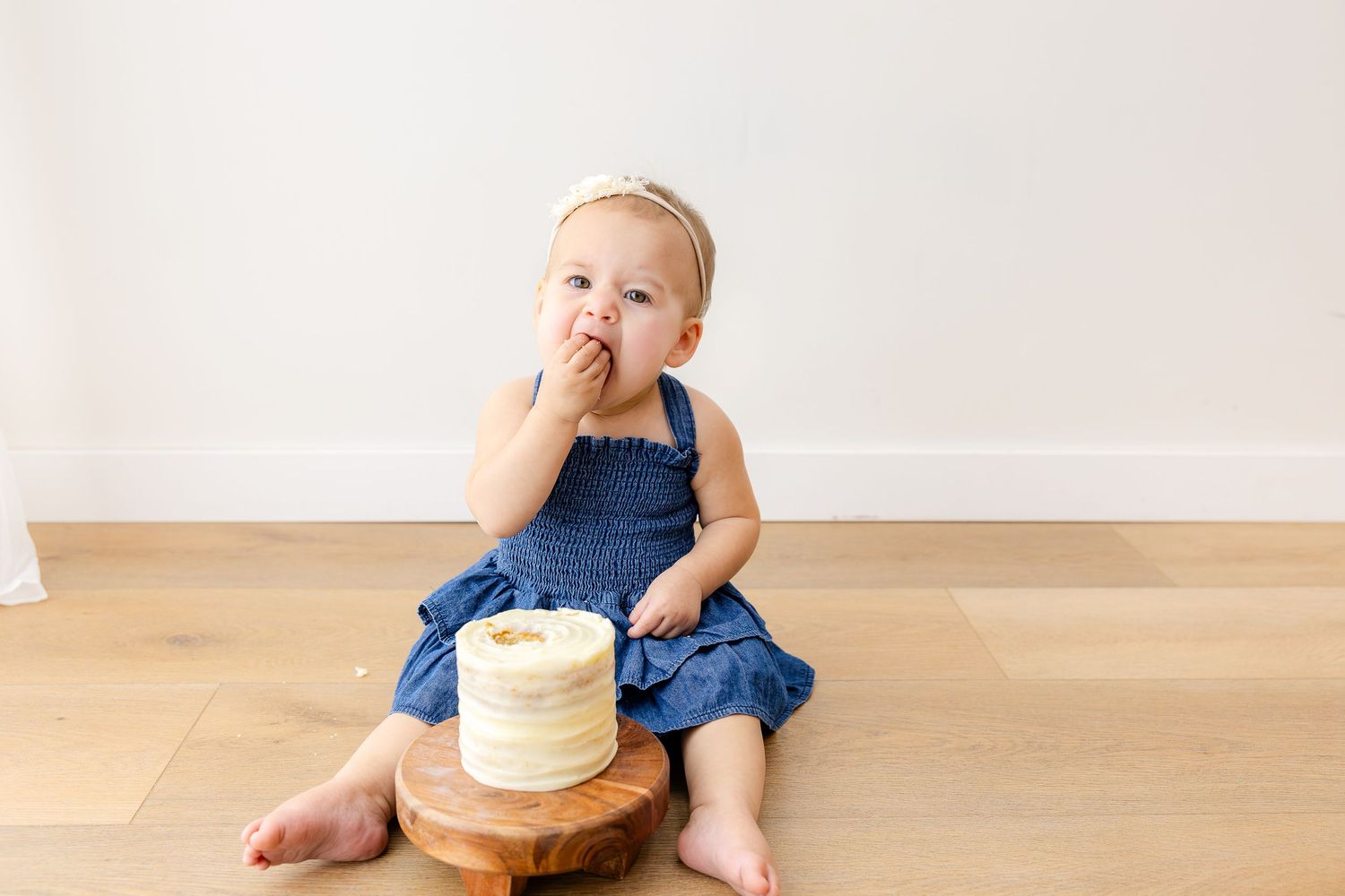 Small hands reach down to touch frosted turquoise and white cake on wooden surface.