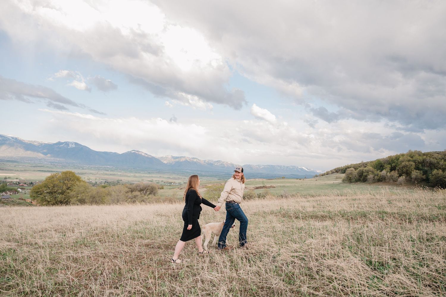 Two people dance together in an open field with mountains and cloudy skies in the background.