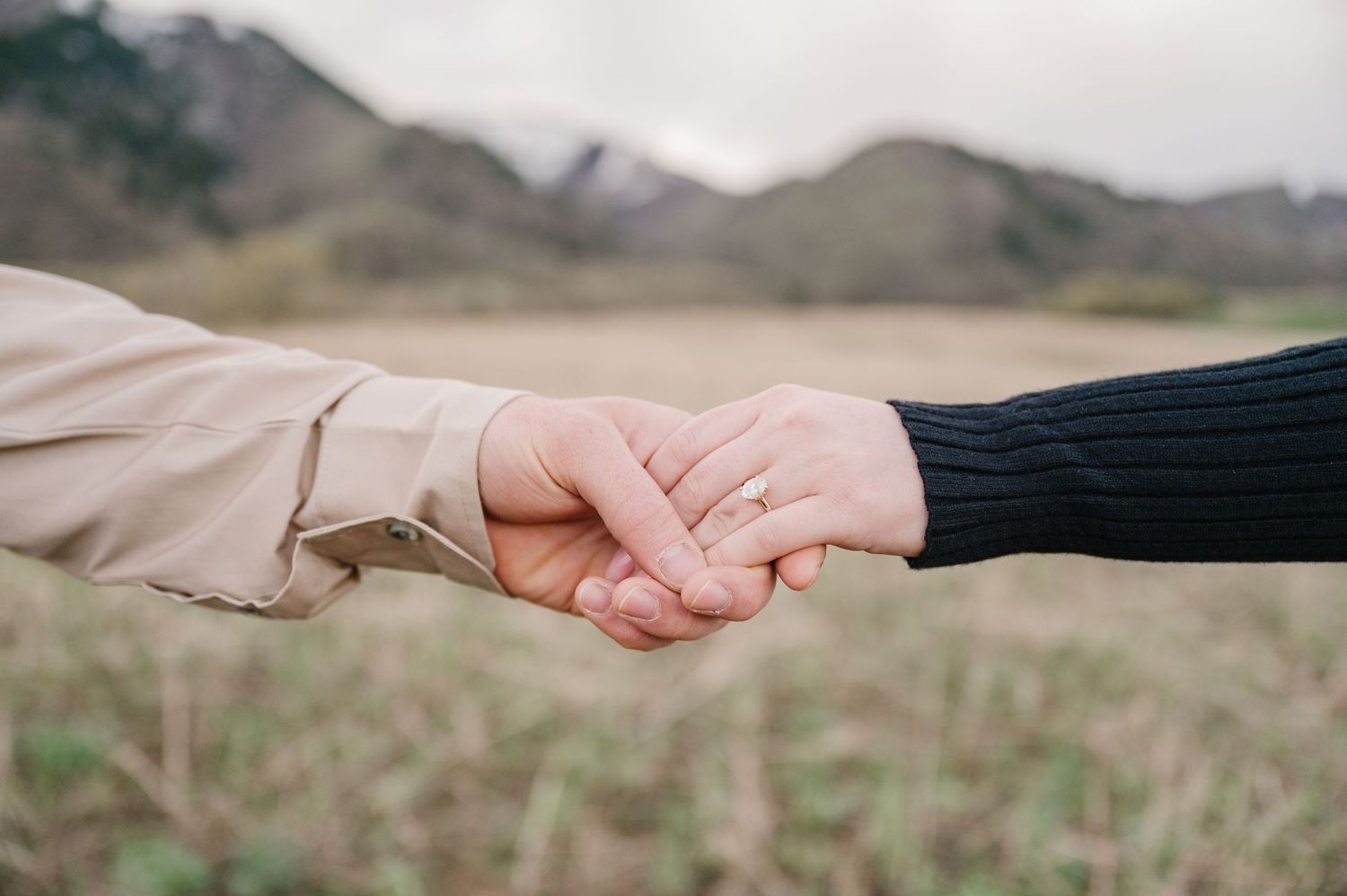 Two people holding hands against a blurred mountain landscape backdrop.