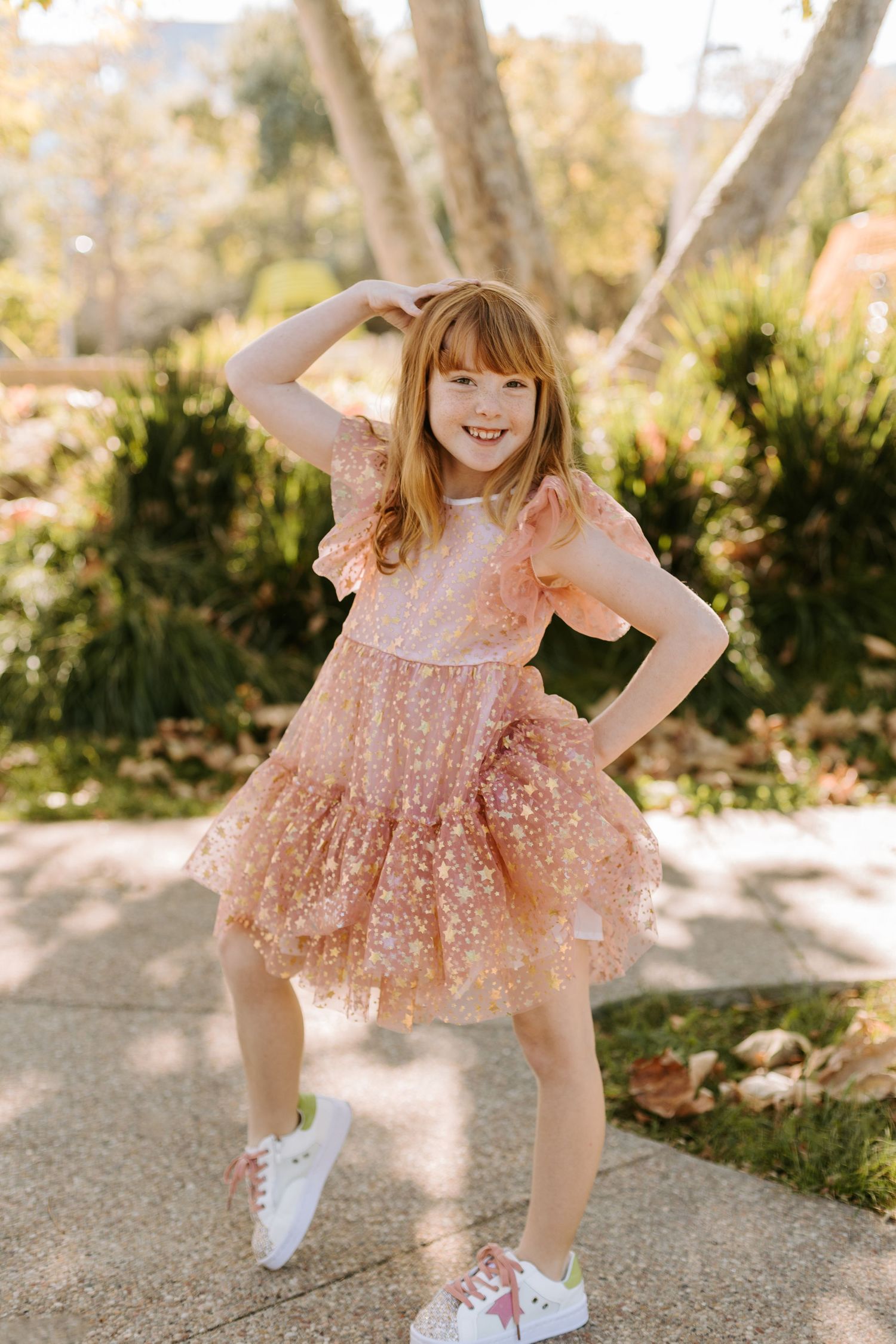 A girl smiling and posing wearing a pink dress with golden stars.