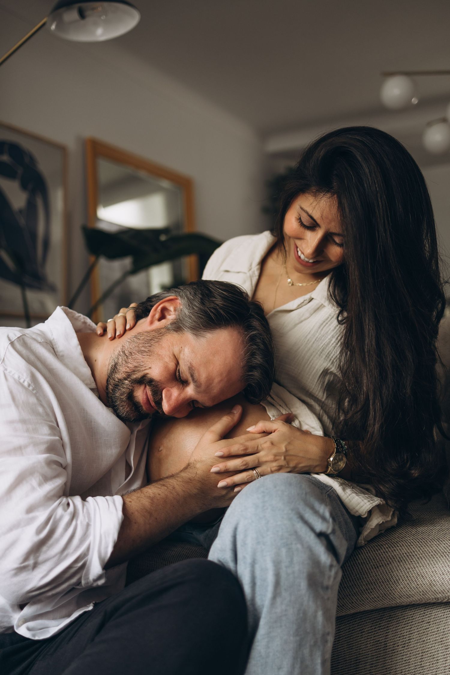 Expectant father tenderly rests his head on pregnant partners belly while she smiles warmly.