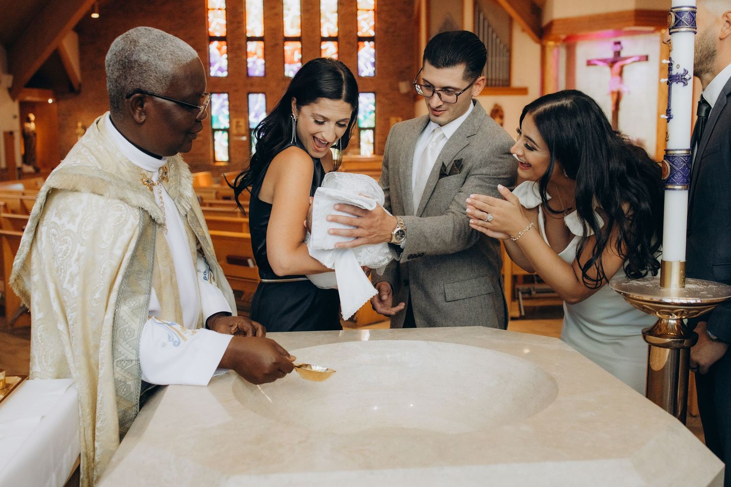 Priest performs a baptism ceremony for a newborn baby surrounded by proud family members in church.