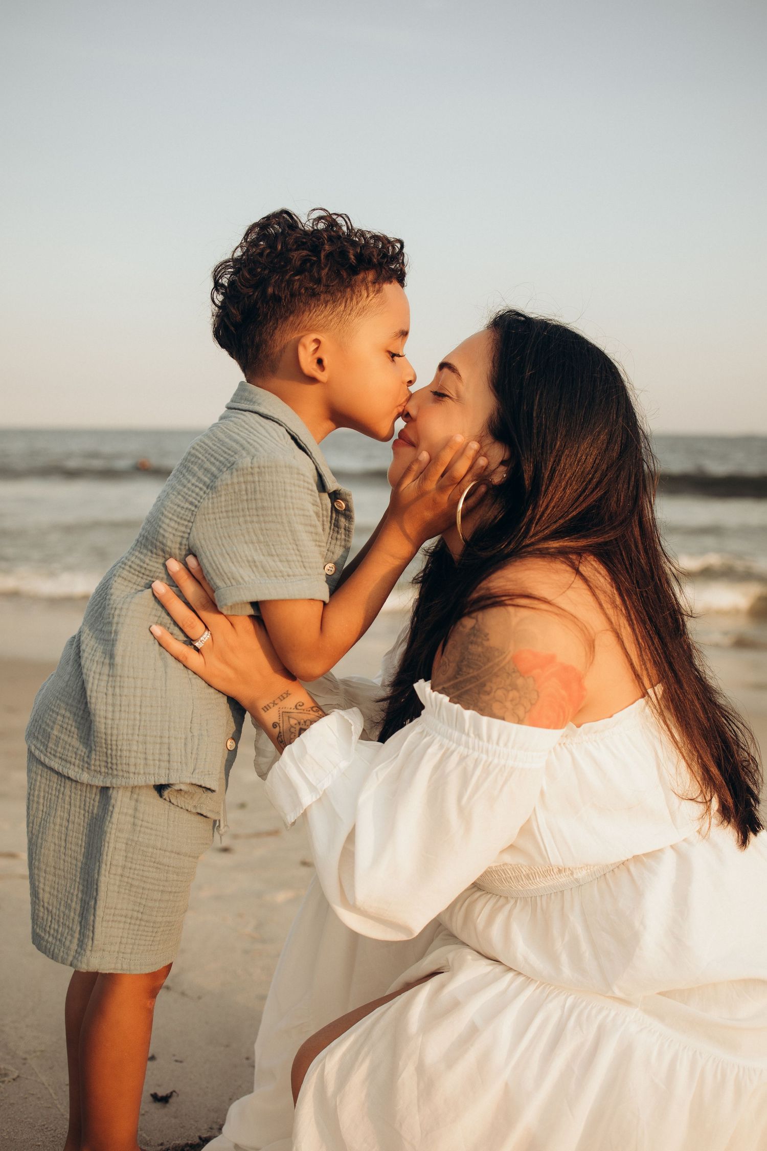 Loving mother receives a kiss from her young son during a beautiful beach sunset photo session.