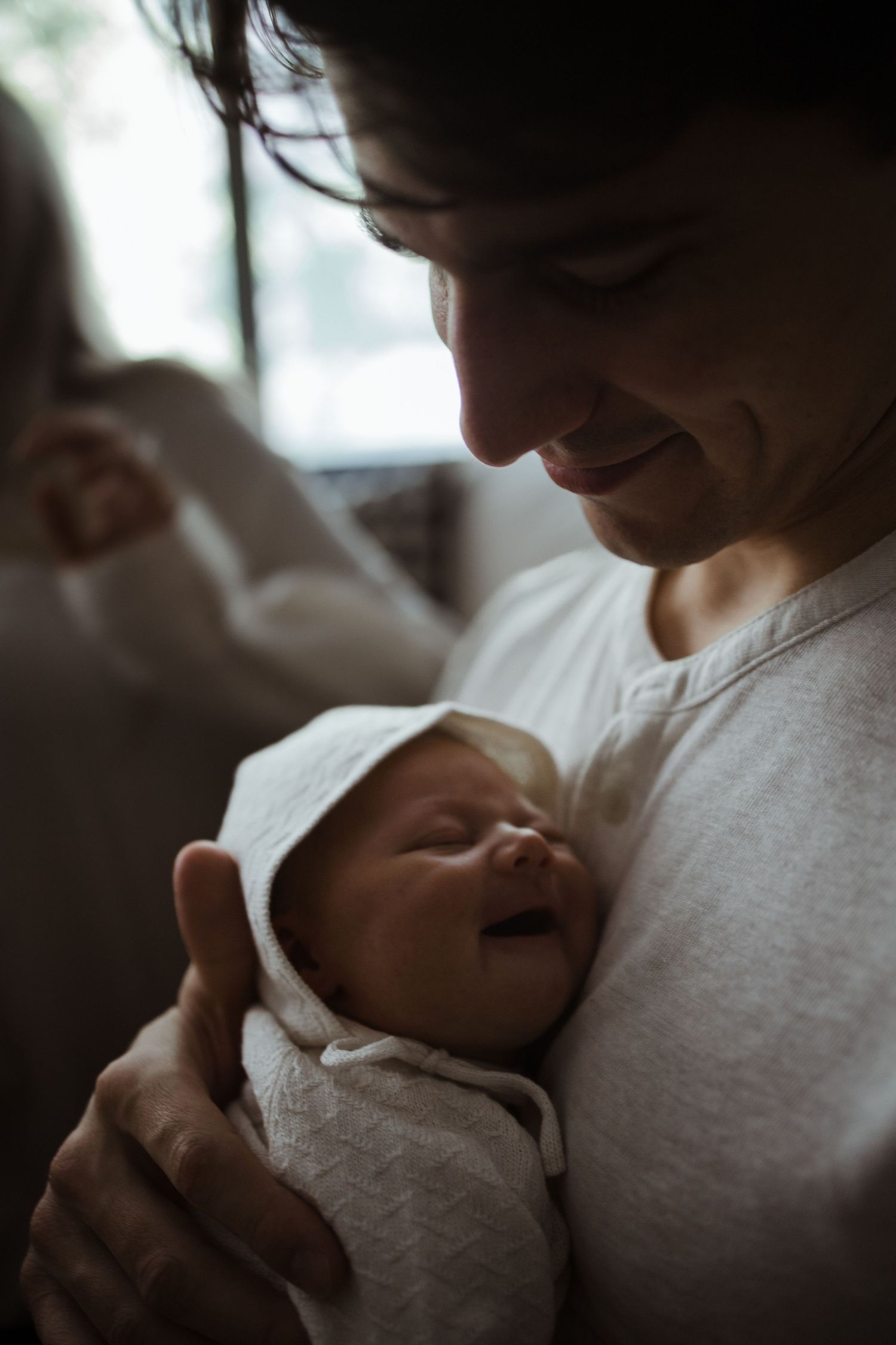 Smiling new father tenderly holding swaddled newborn baby in white wrap indoors.